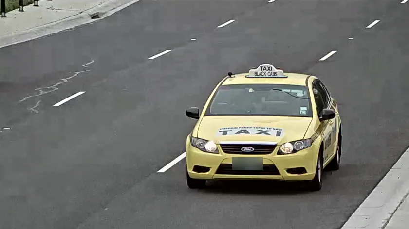 A yellow Ford taxi approaching on a multi-lane road, seen from a camera mounted above the roadside